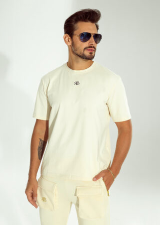 Mężczyzna w beżowym t-shircie OFF od Ricco&Bella z logo RB na klatce piersiowej, noszący okulary przeciwsłoneczne.