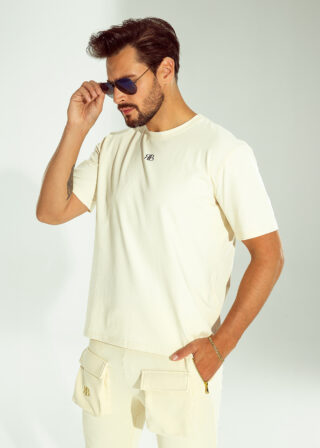 Mężczyzna poprawiający okulary przeciwsłoneczne, ubrany w beżowy t-shirt OFF od Ricco&Bella z logo RB.