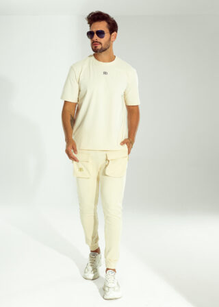 Pełna sylwetka mężczyzny w beżowym zestawie OFF od Ricco&Bella – t-shirt z logo RB i spodnie z kieszeniami.
